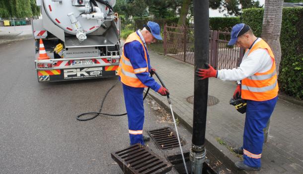 dwaj mężczyźni czyszczą kanalizację deszczową